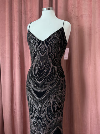 Mannequin wearing a black and silver patterned dress against a pink curtain background