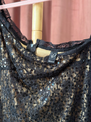 Black sequin dress on a hanger with a visible brand label against a pink background