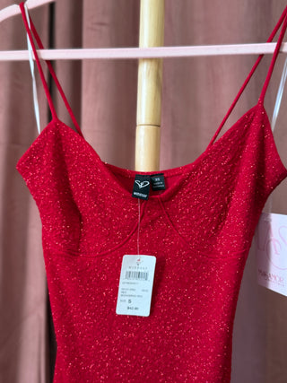 Red sparkly top on a hanger with a visible tag against a brown curtain background